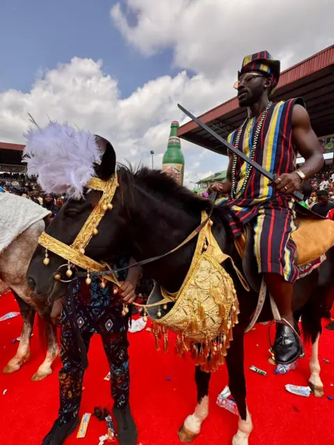 Kyla Herrmannsen / BBC A man on  a horse dressed in golden brocade, standing on a red carpet.
